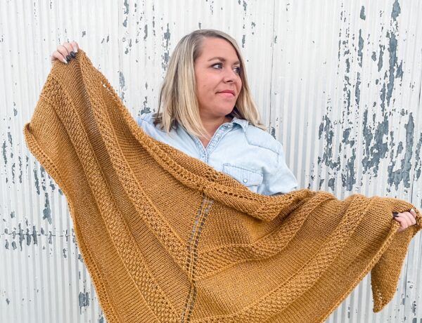 A woman holds an oversized shawl knit in a gold alpaca blend yarn.
